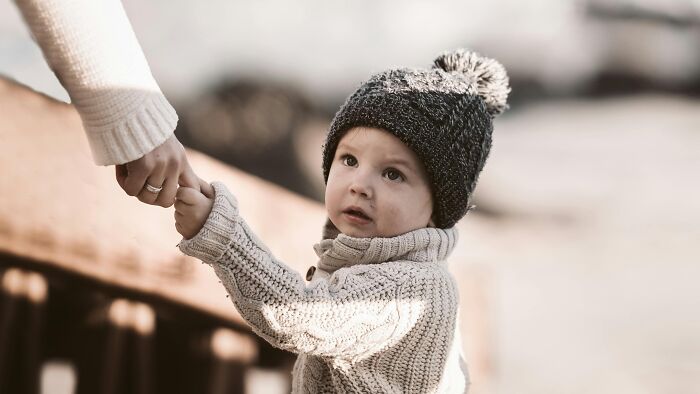 Toddler wearing knitted hat and sweater holding adult’s hand outdoors, illustrating ingenious inventions adapting new purposes.