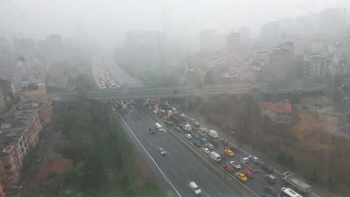 Heavy rain causing traffic jam on highway with city buildings in foggy weather, showcasing wild nature conditions.