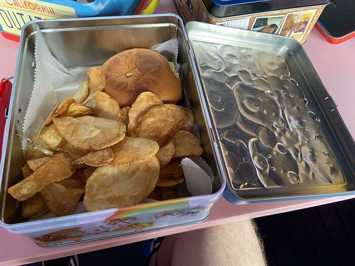 Chips and a sandwich served inside a colorful metal lunchbox, showcasing a ridiculous food serving idea in restaurants.