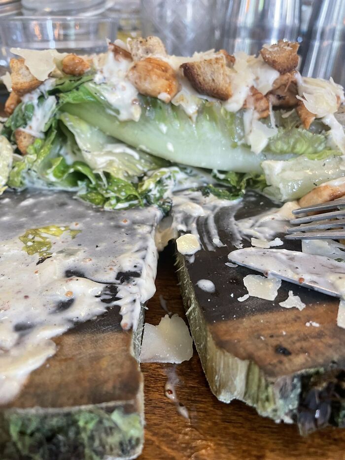 Caesar salad served messily on a broken wooden board, highlighting ridiculous food presentation in restaurants.