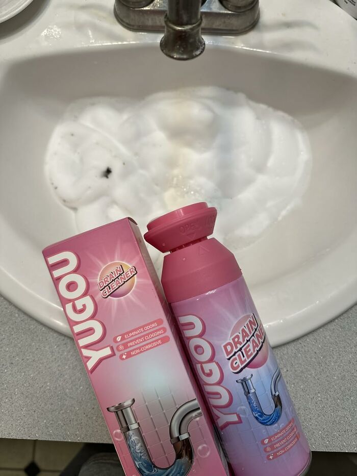 Pink Yugou drain cleaner bottle and box placed on a bathroom sink with foam from cleaning visible in the basin.