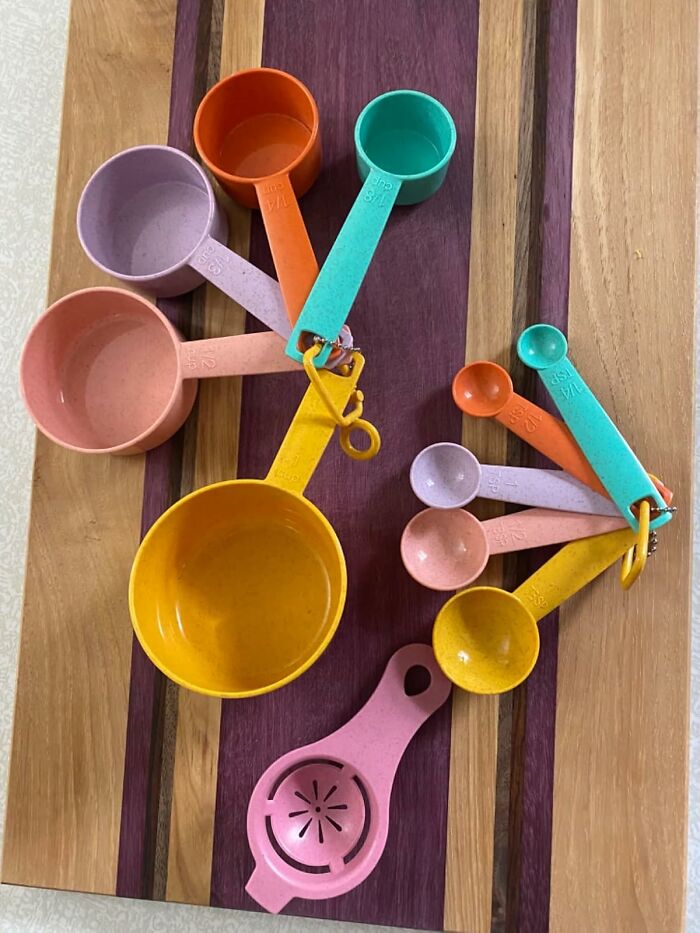 Colorful measuring cups and spoons set with a citrus juicer arranged on a wooden kitchen counter space.