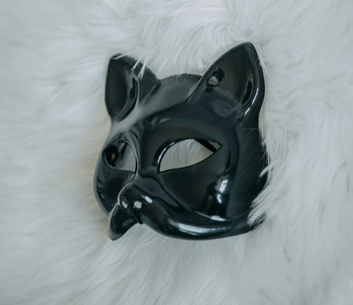 Black cat mask resting on white fur, symbolizing a mysterious figure in a full-body cat suit at night. Black cat mask resting on white fur, symbolizing a mysterious figure in a full-body cat suit at night.