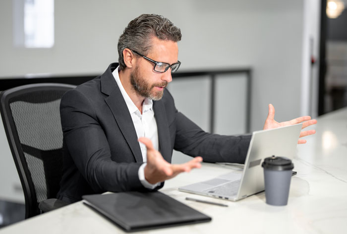 Man in a suit looking frustrated at laptop, illustrating boss told guy to message after every client situation.