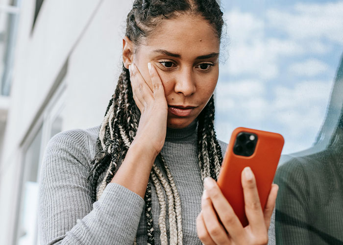 Woman rethinks her relationship with boyfriend looking worried and holding phone near a window in daytime setting Woman rethinks her relationship with boyfriend looking worried and holding phone near a window in daytime setting