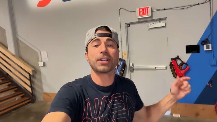 Man wearing a NASA shirt and backward cap, speaking indoors with people share unsubscribed YouTubers concept.
