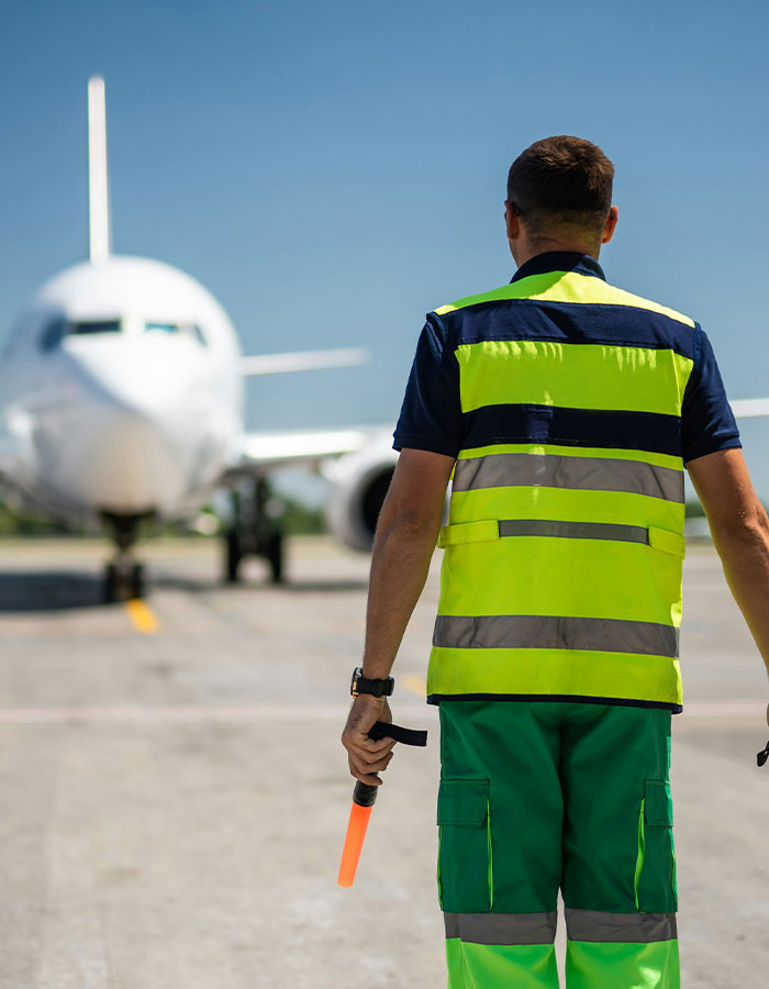 Airport ground crew member in high-visibility vest directing airplane before emergency landing caused by passenger scare on flight. Airport ground crew member in high-visibility vest directing airplane before emergency landing caused by passenger scare on flight.