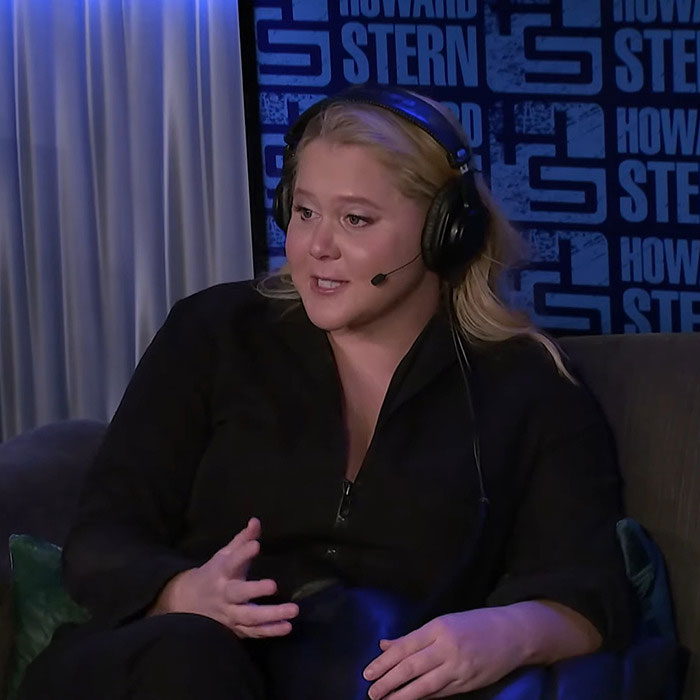 Amy Schumer wearing headset and black outfit, discussing weight loss jab on Howard Stern show set with blue background. Amy Schumer wearing headset and black outfit, discussing weight loss jab on Howard Stern show set with blue background.