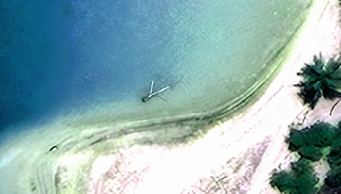Aerial view of a shoreline with a large object partially submerged in water, related to Amelia Earhart mystery. Aerial view of a shoreline with a large object partially submerged in water, related to Amelia Earhart mystery.