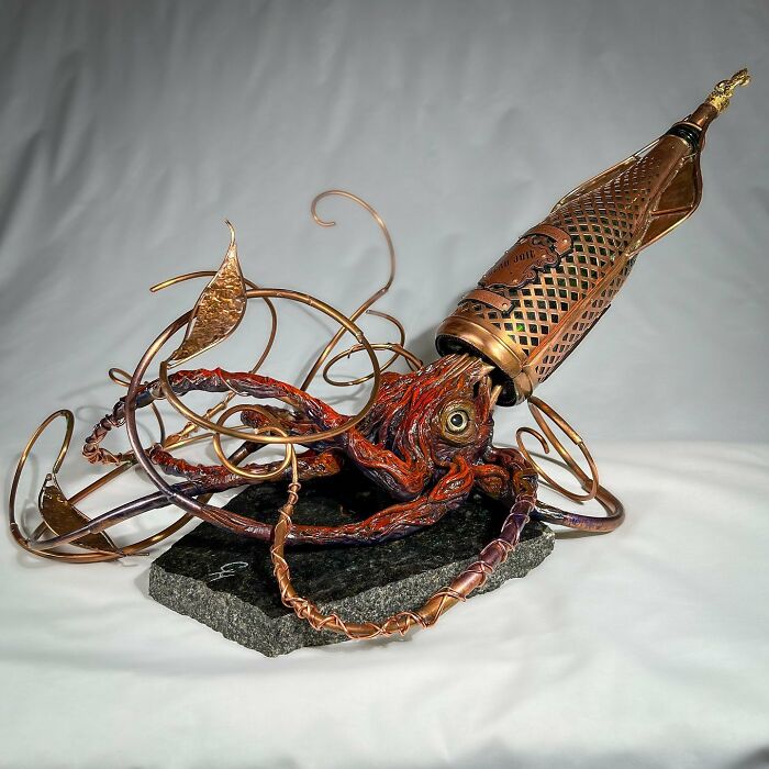 Scrap metal animal sculpture of an intricately designed squid with tentacles and a detailed metallic body on a stone base.