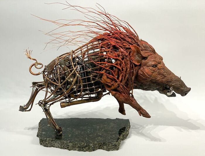 Striking scrap metal animal sculpture of a running boar with detailed metalwork and textured mane on stone base.
