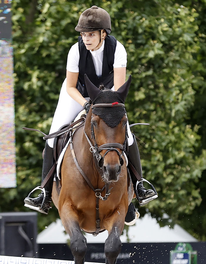 Athina Onassis riding a horse during an equestrian event, wearing a helmet and white riding clothes outdoors. Athina Onassis riding a horse during an equestrian event, wearing a helmet and white riding clothes outdoors.
