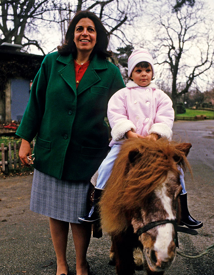 Woman standing next to a child riding a pony outdoors, highlighting reclusive billionaire Athina Onassis in rare appearance. Woman standing next to a child riding a pony outdoors, highlighting reclusive billionaire Athina Onassis in rare appearance.