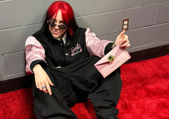 Billie Eilish sitting on red carpet with sunglasses and holding an envelope, fans buzzing about nepo baby discovery. Billie Eilish sitting on red carpet with sunglasses and holding an envelope, fans buzzing about nepo baby discovery.
