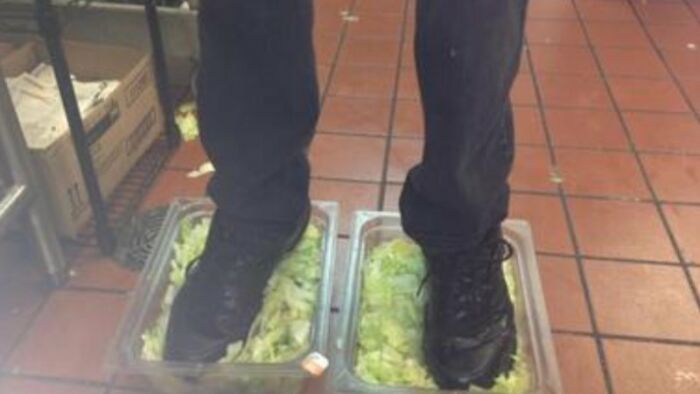 Person standing with black shoes in containers filled with lettuce, demonstrating unusual things people did in public.