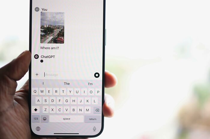 Hand holding smartphone showing ChatGPT conversation where user asks where they are, highlighting AI manipulation concerns.