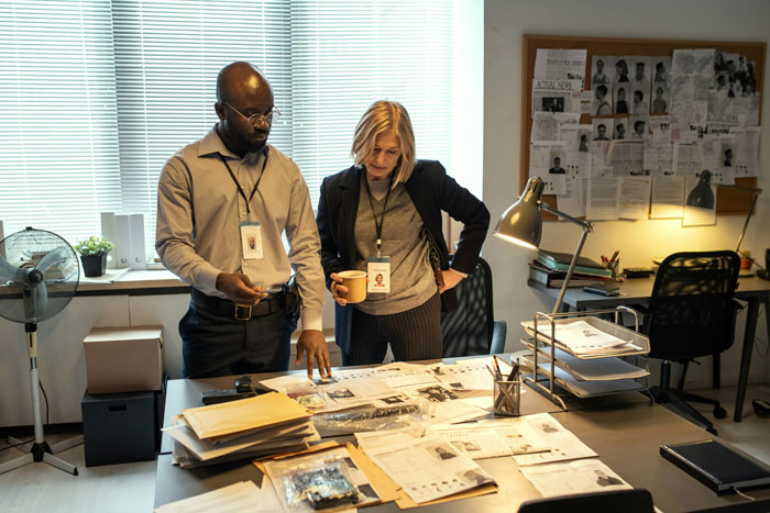 Two FBI agents reviewing documents and photos in an office related to DB Cooper investigation files. Two FBI agents reviewing documents and photos in an office related to DB Cooper investigation files.