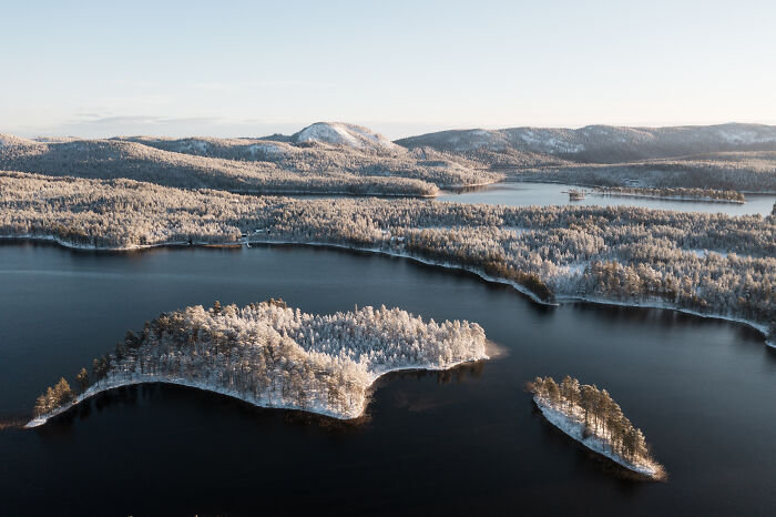 Aerial view of a snowy forested cabin in the woods surrounded by a calm lake, depicting a peaceful true home retreat. Aerial view of a snowy forested cabin in the woods surrounded by a calm lake, depicting a peaceful true home retreat.