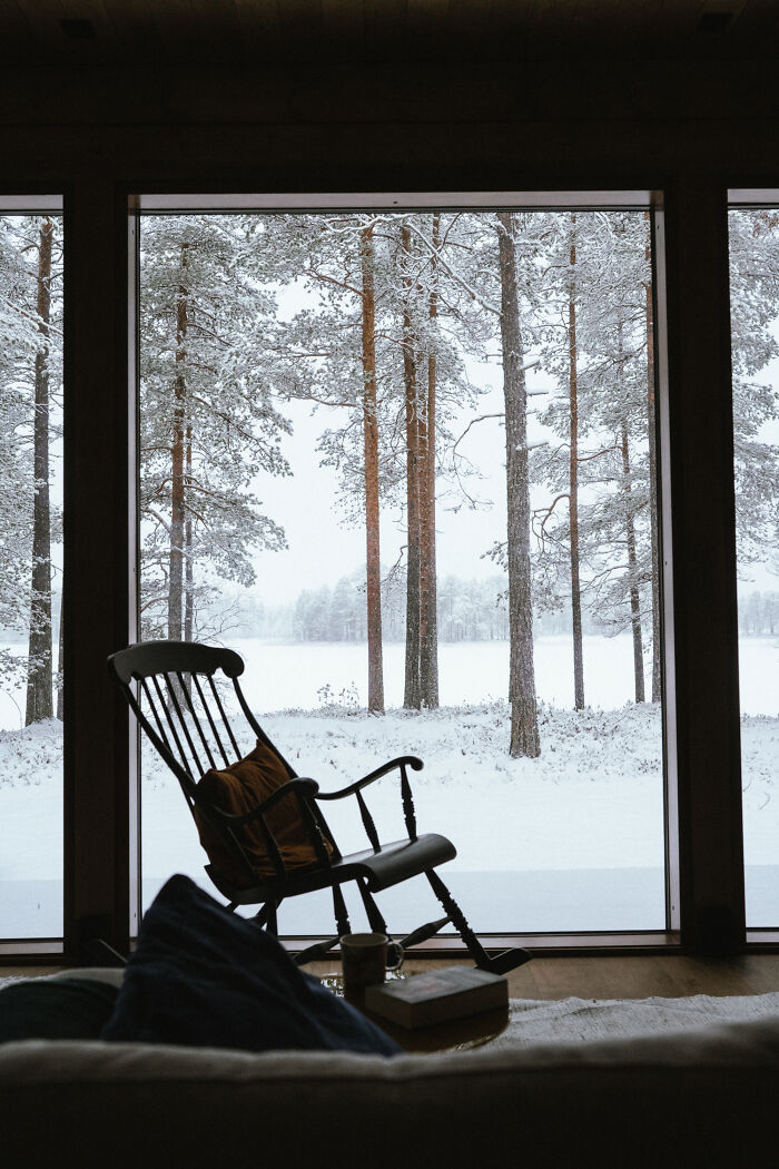 Cozy cabin interior with rocking chair facing snowy woods, showcasing peaceful cabin in the woods retreat and nature views. Cozy cabin interior with rocking chair facing snowy woods, showcasing peaceful cabin in the woods retreat and nature views.