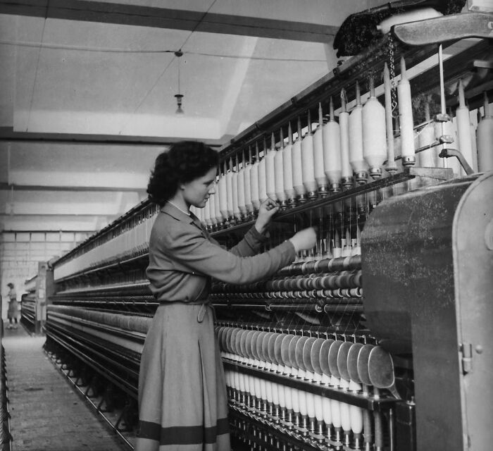 Woman operating textile machinery in a factory, daily life photo from the 50s capturing global industrial work scenes.