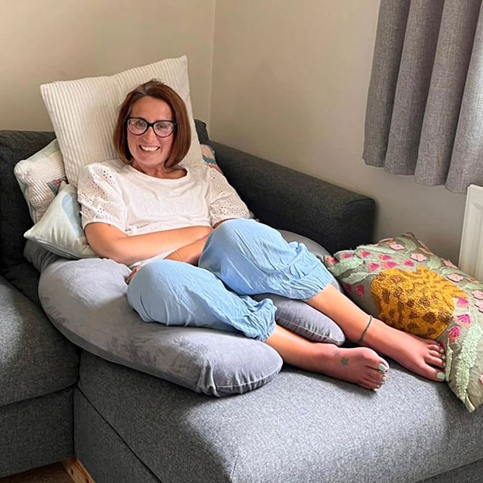 Woman with glasses smiling while sitting on a gray sofa, illustrating a mom ends her life by starving story. Woman with glasses smiling while sitting on a gray sofa, illustrating a mom ends her life by starving story.