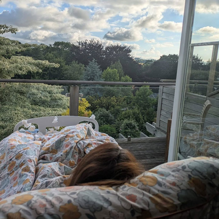 Woman lying in bed on balcony overlooking trees and cloudy sky, symbolizing mom ends life by starving to protect kids. Woman lying in bed on balcony overlooking trees and cloudy sky, symbolizing mom ends life by starving to protect kids.