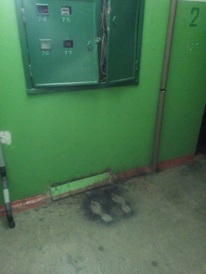 Faded footprints on a dirty floor beneath an open green electrical panel in a dimly lit hallway cursed image.
