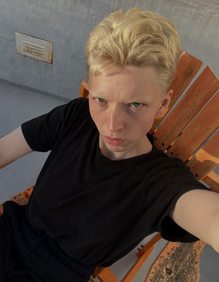 Model with short blonde hair sitting in an orange chair, reflecting on transitioning and detransitioning experience. Model with short blonde hair sitting in an orange chair, reflecting on transitioning and detransitioning experience.