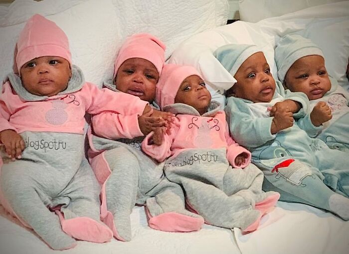 Five of the world’s first surviving nonuplets dressed in colorful outfits lying on a white bed. Five of the world’s first surviving nonuplets dressed in colorful outfits lying on a white bed.
