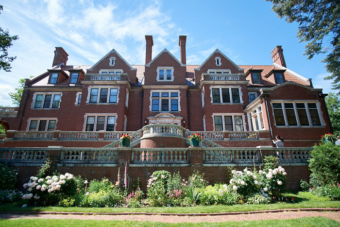 Large historic home with red brick facade, multiple chimneys, and a landscaped garden, showcasing American architectural heritage.
