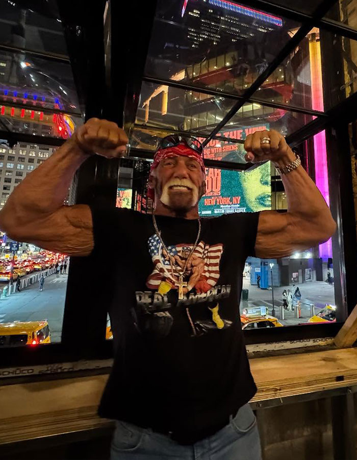 WWE legend Hulk Hogan flexing muscles indoors at night with city lights and billboards in the background. WWE legend Hulk Hogan flexing muscles indoors at night with city lights and billboards in the background.