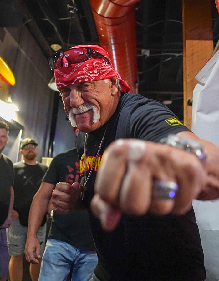 WWE legend Hulk Hogan wearing red bandana and black shirt, making a fist gesture in an indoor setting. WWE legend Hulk Hogan wearing red bandana and black shirt, making a fist gesture in an indoor setting.