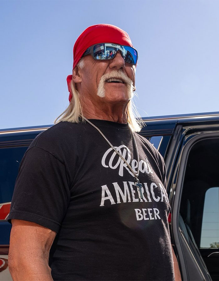 WWE legend Hulk Hogan wearing sunglasses and a red bandana, standing outside near a vehicle on a sunny day. WWE legend Hulk Hogan wearing sunglasses and a red bandana, standing outside near a vehicle on a sunny day.