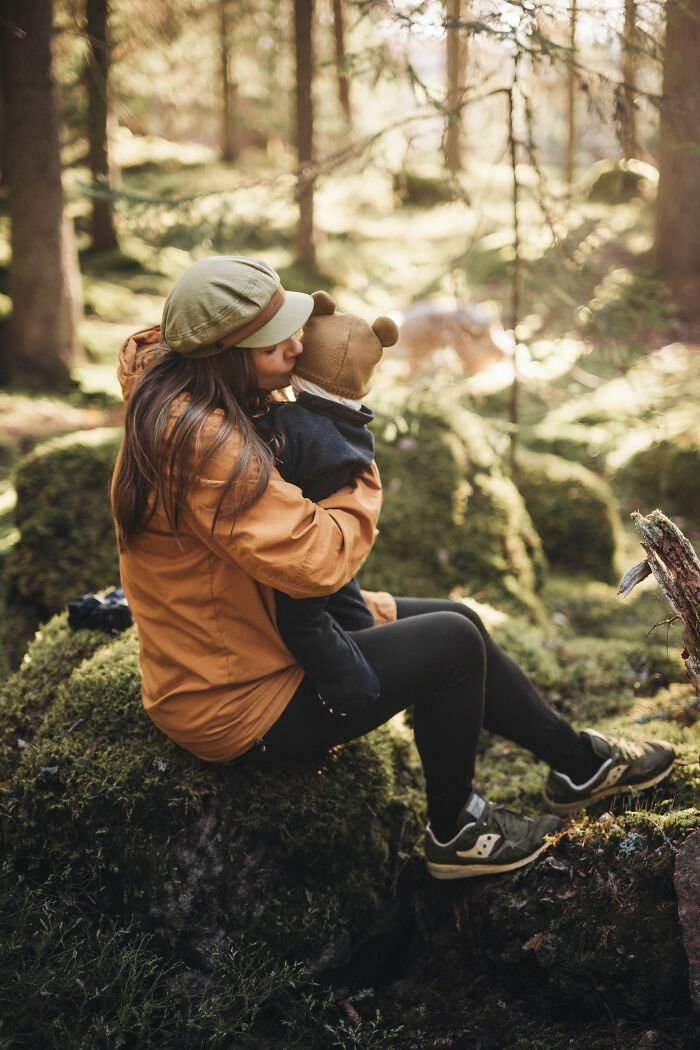 Woman sitting on mossy rock in the woods, holding a child, enjoying peaceful cabin life in nature’s quiet embrace. Woman sitting on mossy rock in the woods, holding a child, enjoying peaceful cabin life in nature’s quiet embrace.