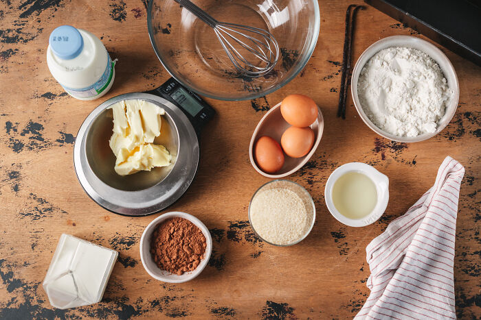 Baking ingredients including eggs, flour, butter, cocoa powder, and milk on a wooden table for childhood cake recipe. Baking ingredients including eggs, flour, butter, cocoa powder, and milk on a wooden table for childhood cake recipe.