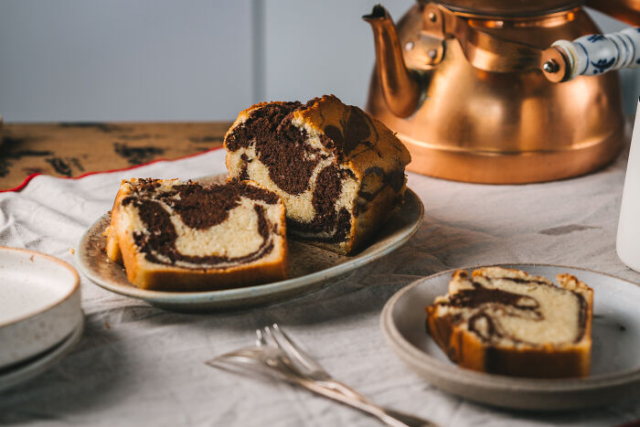 Marble childhood cake sliced on plates next to vintage teapot, symbolizing family remedy after hospital trip. Marble childhood cake sliced on plates next to vintage teapot, symbolizing family remedy after hospital trip.