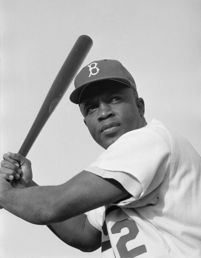 Black baseball player in 1950s uniform holding bat, capturing daily life across the globe in the 50s.