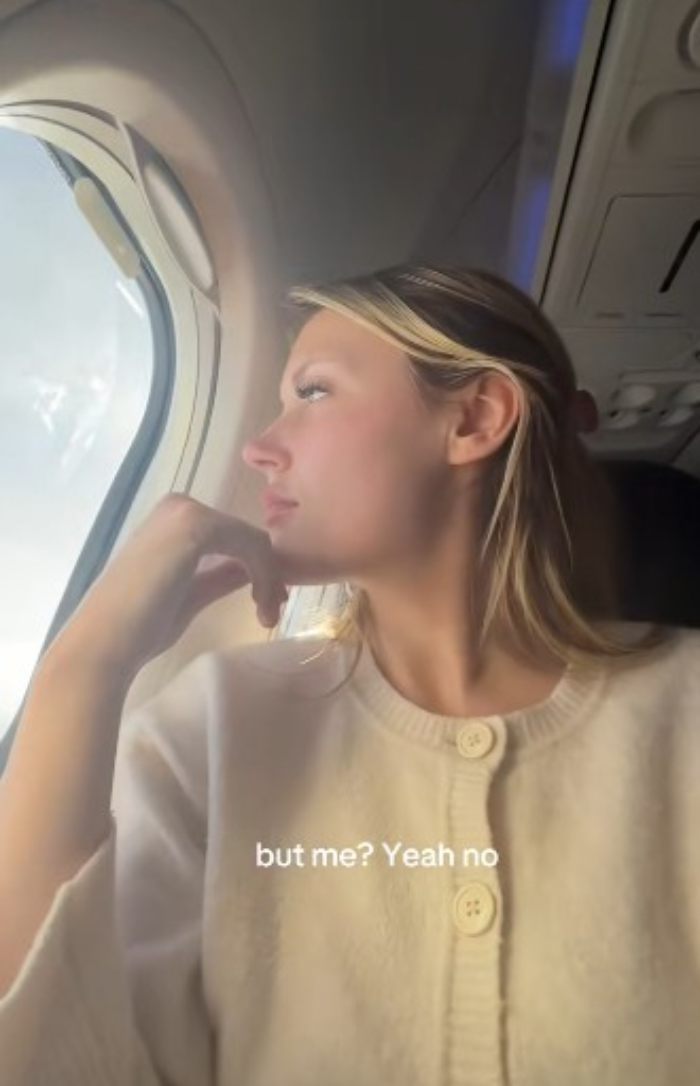 Young woman looking out airplane window, reflecting on plastic surgery recovery and its complications. Young woman looking out airplane window, reflecting on plastic surgery recovery and its complications.