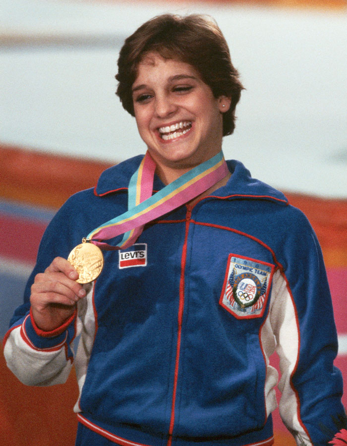 Olympic gold medalist Mary Lou Retton smiling with gold medal, wearing Team USA jacket during award ceremony. Olympic gold medalist Mary Lou Retton smiling with gold medal, wearing Team USA jacket during award ceremony.