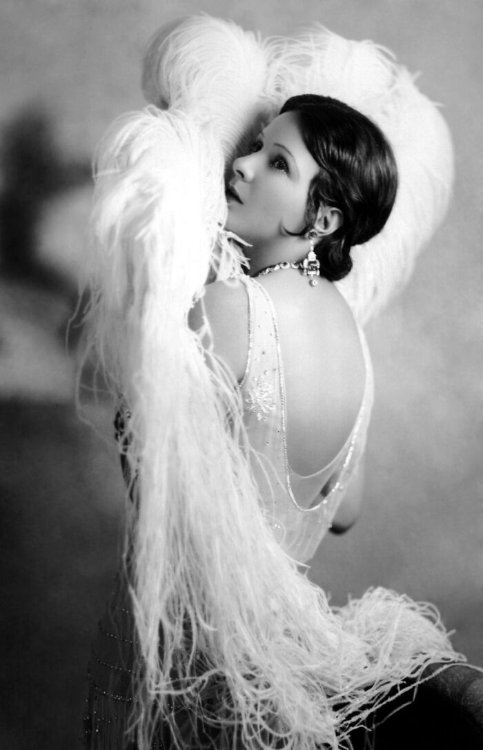 Vintage black and white portrait of a woman with feathers, showcasing timeless beauty from century-old photos.