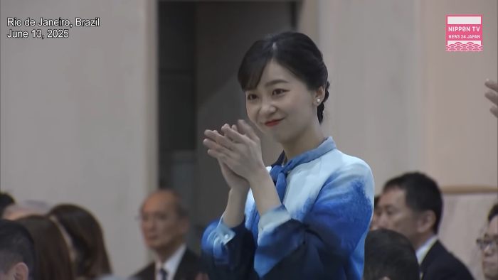 Japanese Princess Kako smiling and applauding at an indoor event, surrounded by seated attendees in formal attire. Japanese Princess Kako smiling and applauding at an indoor event, surrounded by seated attendees in formal attire.