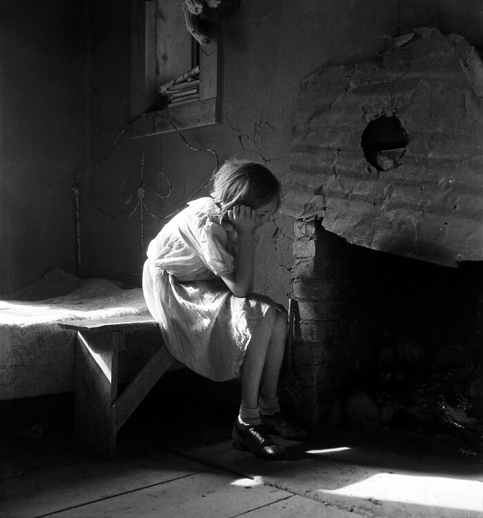 Young girl sitting by a fireplace in a worn room, a somber photo capturing a gut-wrenching moment from history.