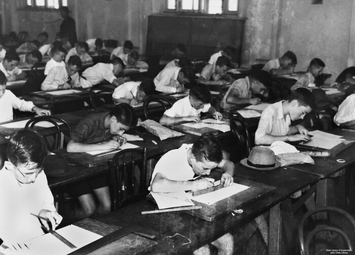 Black and white image of students in a World War II classroom drawing and writing during a school session worldwide.