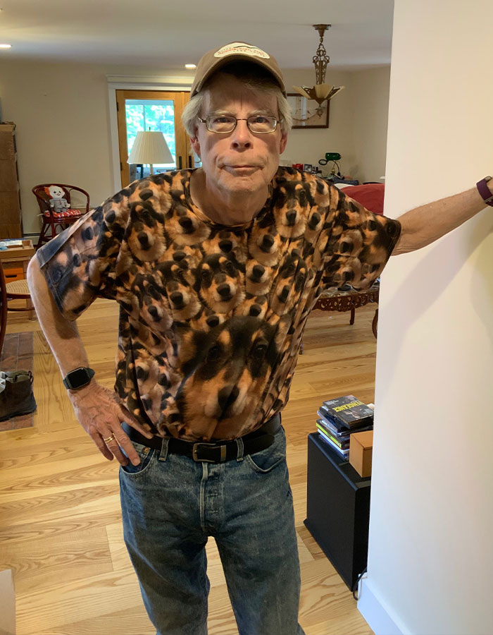 Stephen King standing indoors wearing a dog-patterned shirt and glasses, related to Epstein list conspiracy theories. Stephen King standing indoors wearing a dog-patterned shirt and glasses, related to Epstein list conspiracy theories.
