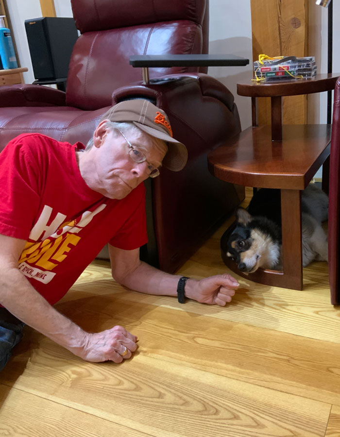 Man in red shirt and cap lying on wooden floor next to a dog under a table, related to Stephen King's Epstein list tweet. Man in red shirt and cap lying on wooden floor next to a dog under a table, related to Stephen King's Epstein list tweet.