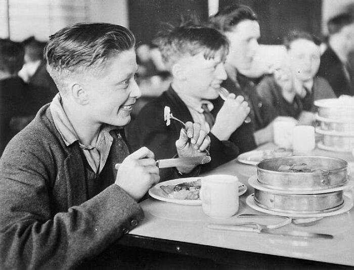 Boys eating lunch together in a school cafeteria during World War II, showcasing daily life in schools worldwide.