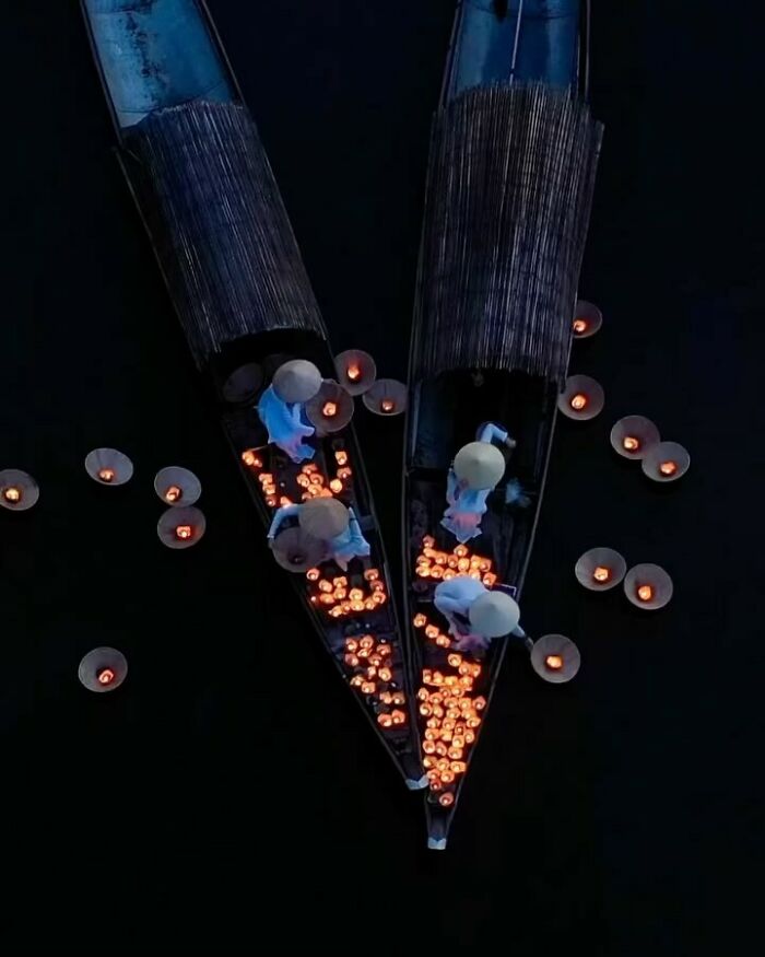 Aerial view of boats with people releasing glowing lanterns on dark water capturing the soul of Asia.
