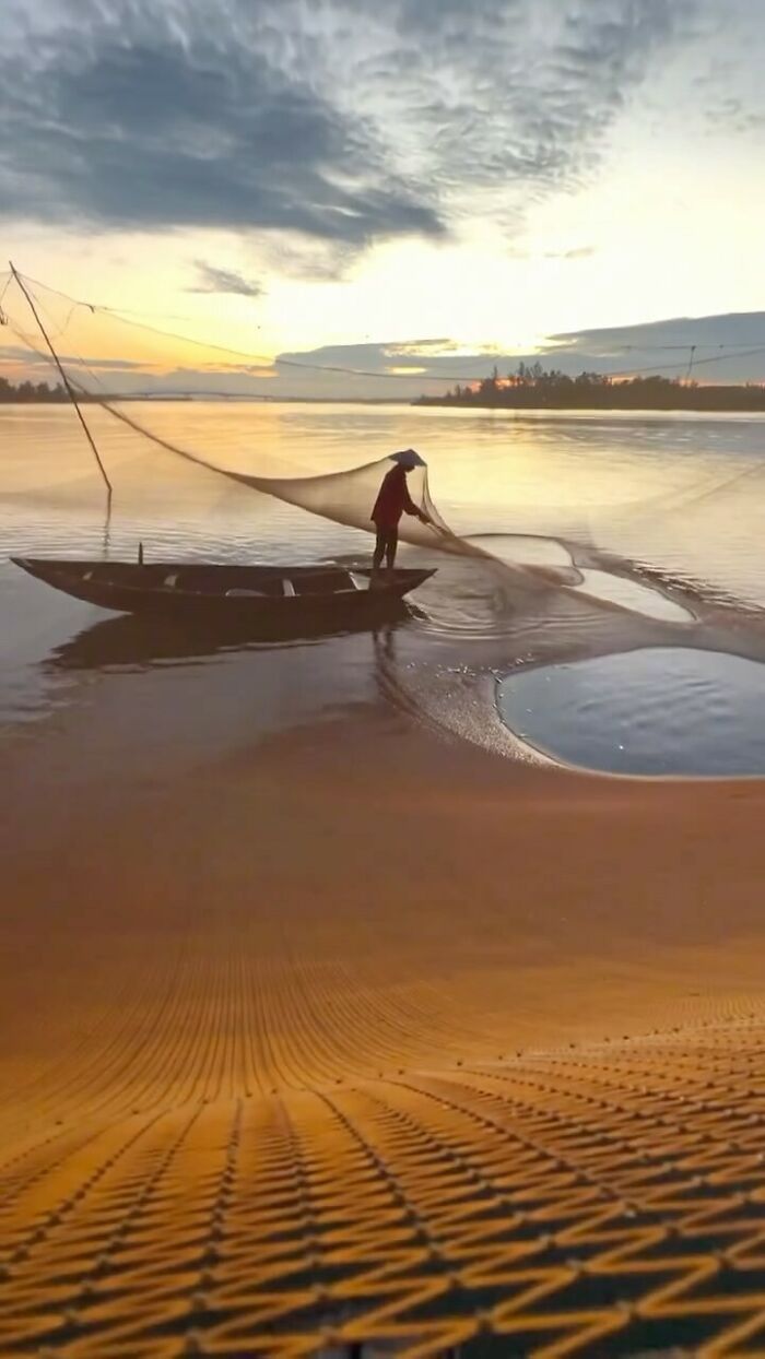 Fisherman casting net from boat on calm water at sunset, capturing the soul of Asia in a stunning landscape photo.