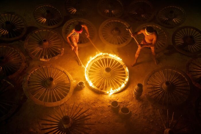 Two men working with large wooden wheels around a fire, capturing the soul of Asia in a stunning cultural scene.
