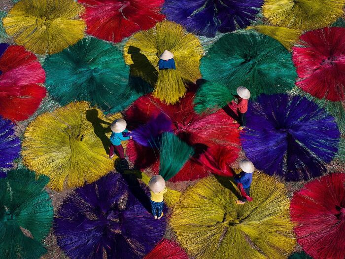 Workers in traditional hats arranging vibrant colored fibers outdoors, capturing the soul of Asia in a stunning photo.